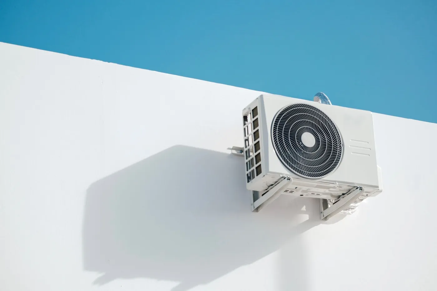 Unidad exterior de aire acondicionado montada sobre un muro blanco.